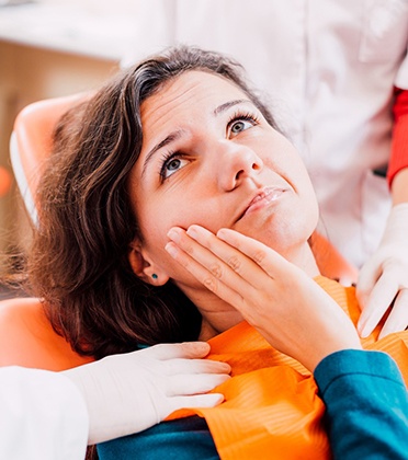 Female dental patient sitting back and rubbing her jaw