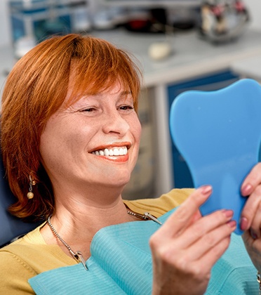 An older woman admiring her dentures in a hand mirror