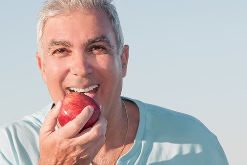Man with dental implants in Norwalk biting an apple.